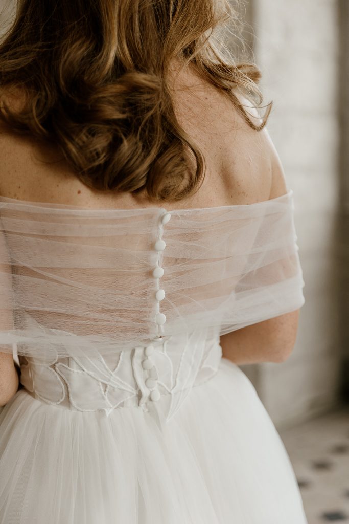 detail du dos de flora et de son cache épaule en tulle fermé par des petits boutons